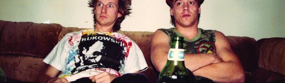 Two men sitting on a couch, with a beer bottle in the foreground.