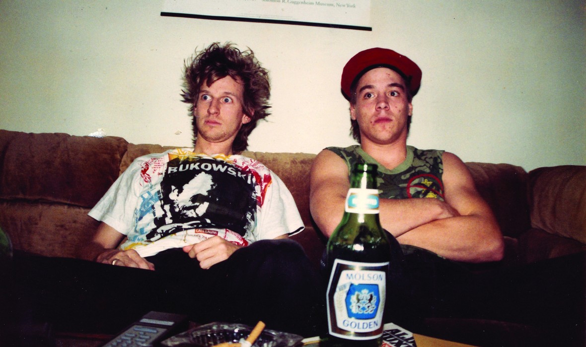 Two men sitting on a couch, with a beer bottle in the foreground.