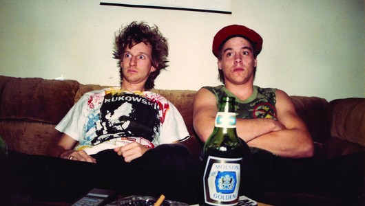 Two men sitting on a couch, with a beer bottle in the foreground.